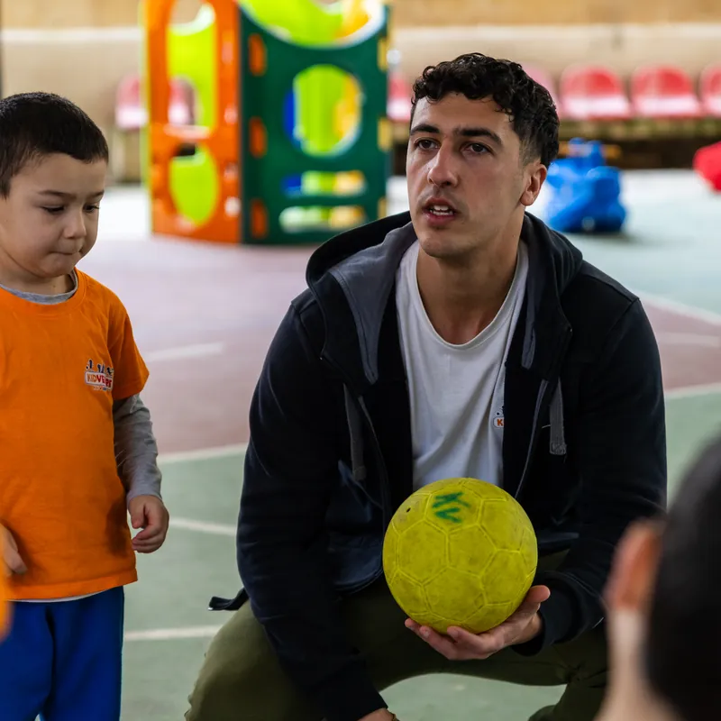 A KidVenture coach crouching with a ball to explain a game