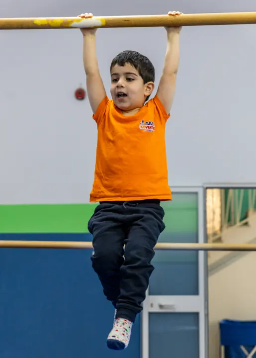 A boy hanging from a gymnastics bar