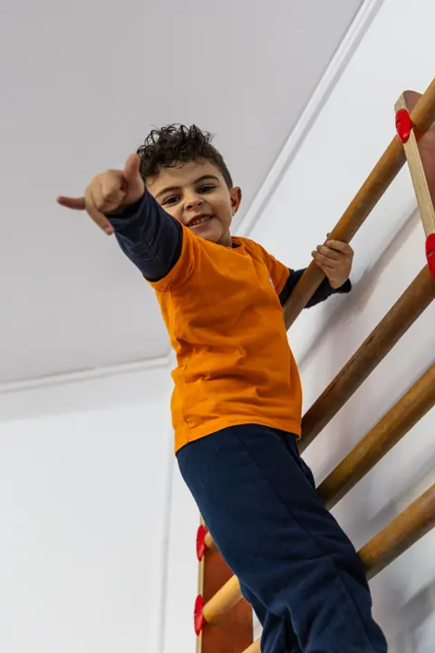 A boy on the wall bars giving a thumbs up