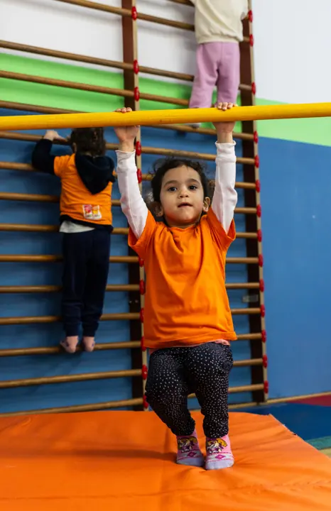 A girl hanging from a bar in front of the wall bars