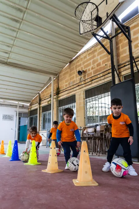 Children dribbling footballs through a line of cones