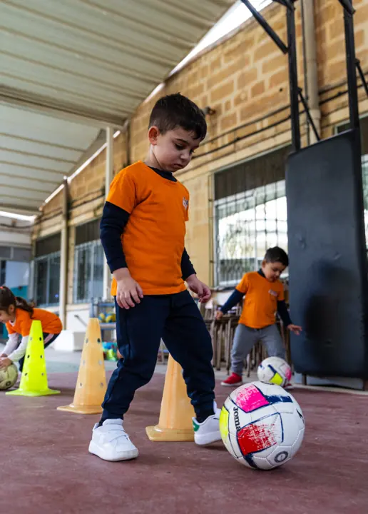 A boy dribbling a football past the cones