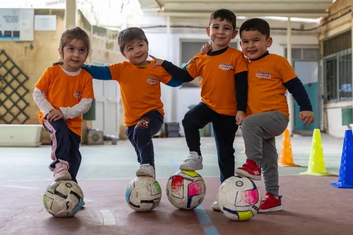 Four children posing with a foot on their footballs