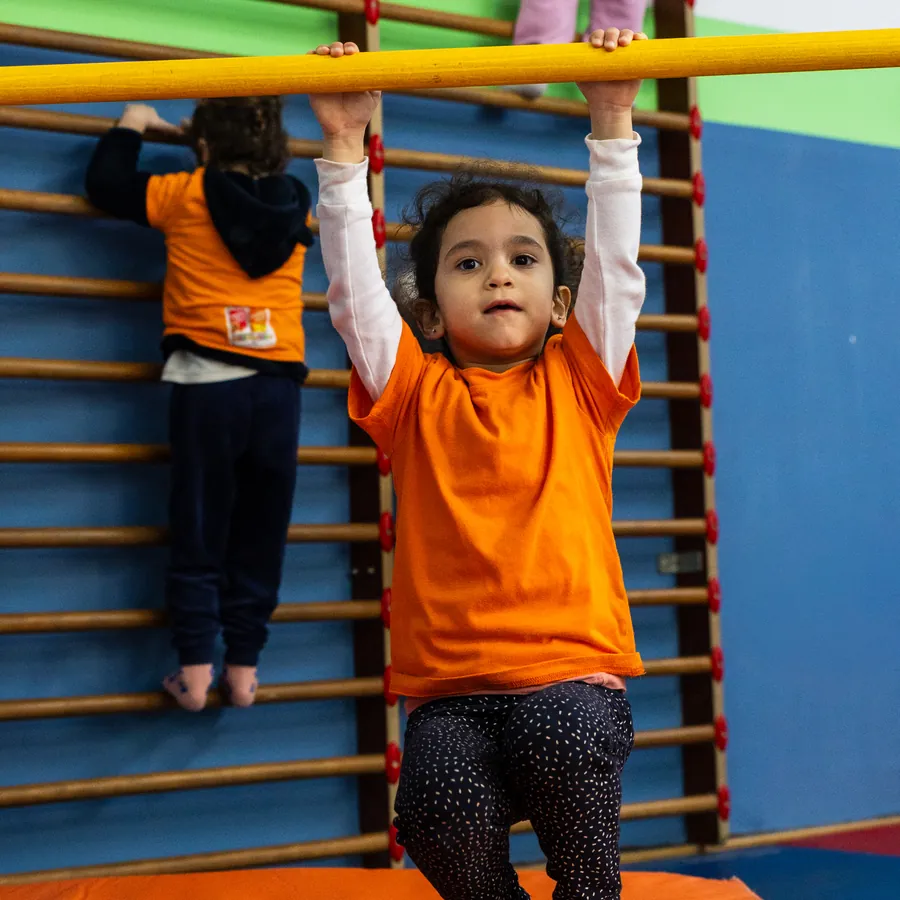 A little girl hanging from a bar in front of the wall bars