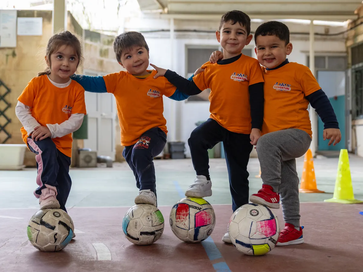 Four children posing with a foot on their footballs